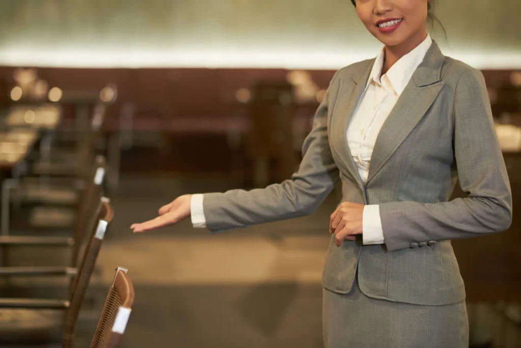 Hostess che accoglie i partecipanti della conferenza con un gesto di benvenuto all'ingresso di una sala congressi